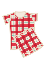 A two-piece kids pyjama set featuring a short-sleeve top and matching shorts in a red, white, and green tartan, with a cream-colored collar, pocket, and drawstring. Made from organic cotton